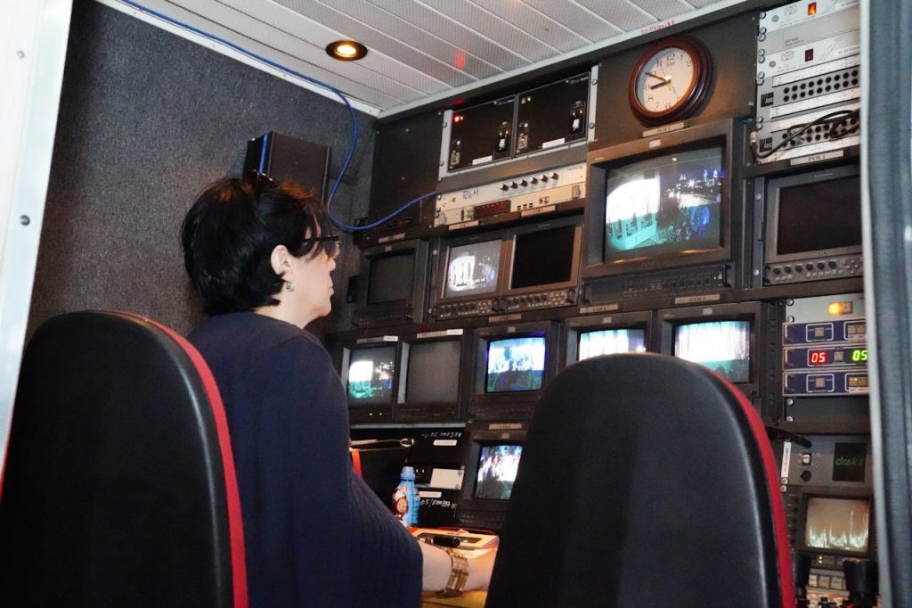 A professional in a TV broadcast control room with multiple screens and equipment.